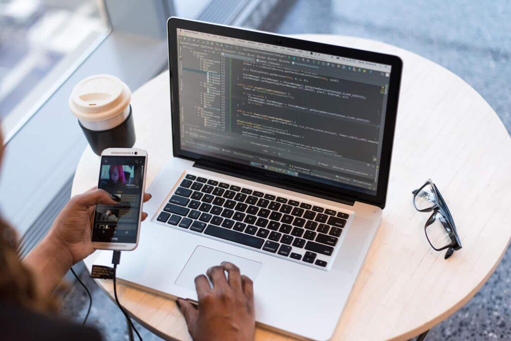 Usuario sentado en una mesa, con celular en la mano y portátil para contactar a CosmoHosting y preguntar acerca de soluciones para una nube segura